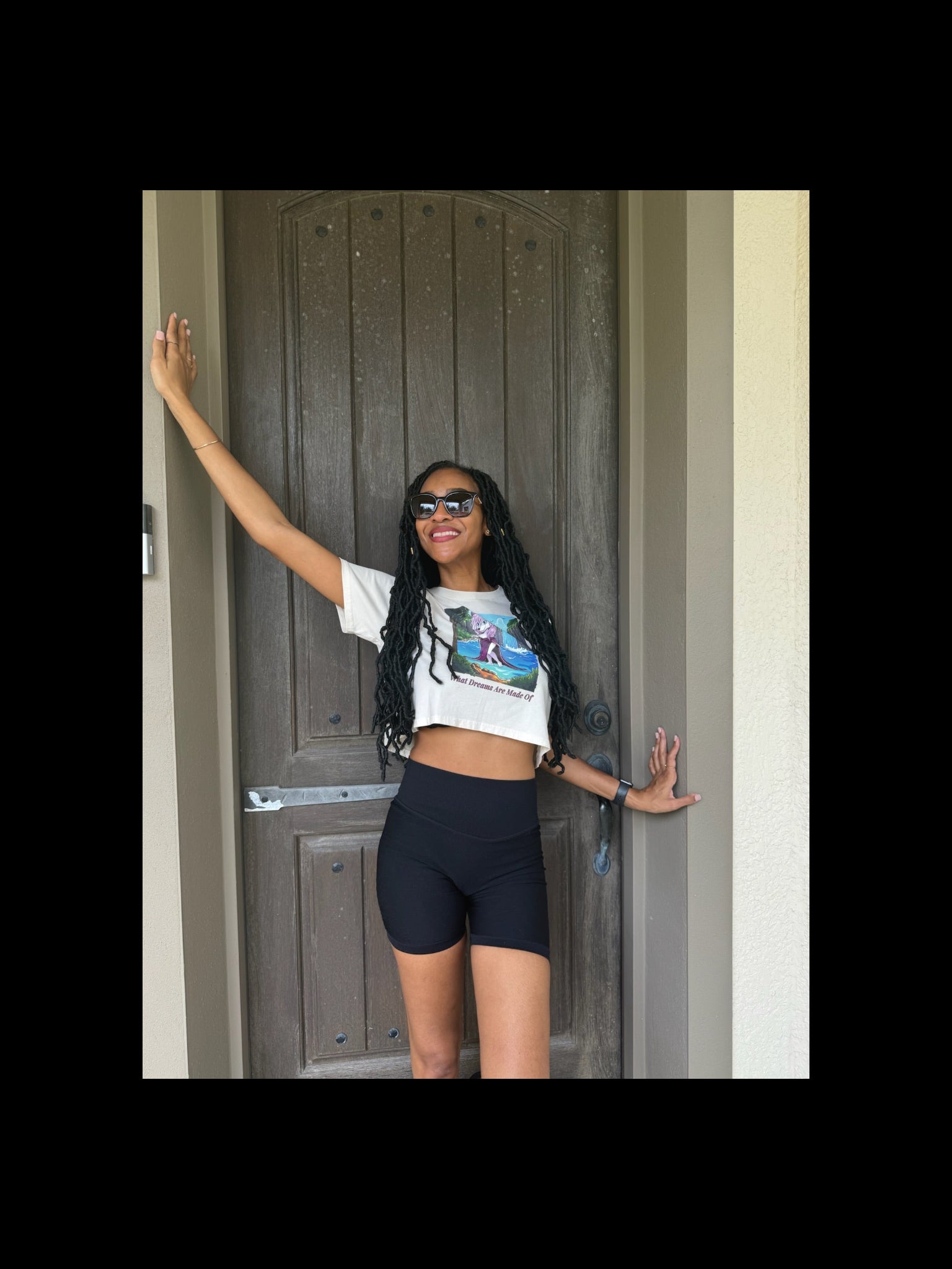 Woman in a white crop top and black shorts standing in front of a door.
